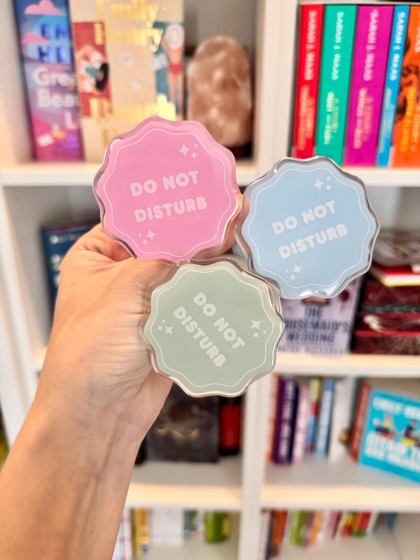 May include: Three acrylic, scalloped-edge signs in pink, blue, and green, each with the words "DO NOT DISTURB" in white. The signs have a star design and are held in front of a bookshelf filled with books.